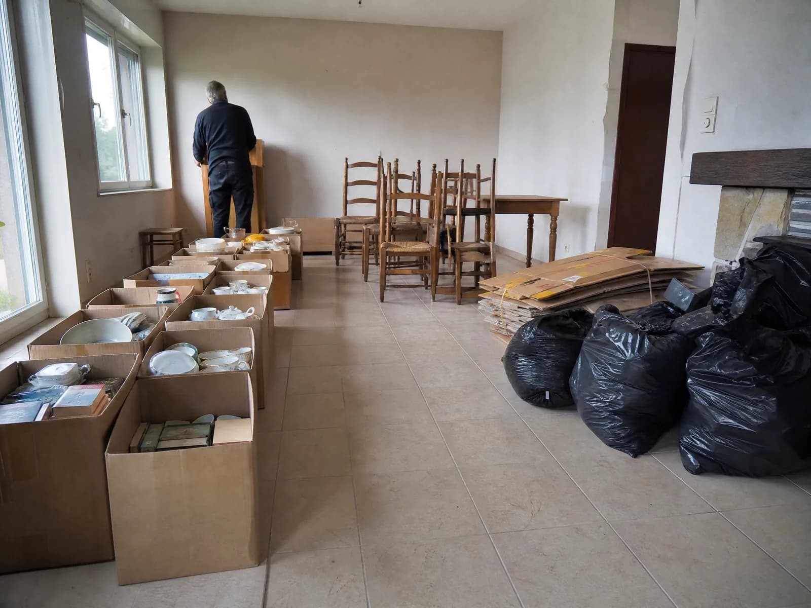Inboedel gesorteerd in een leeggemaakte woonkamer: dozen voor de kringwinkel, oude stoelen, karton en zakken restafval